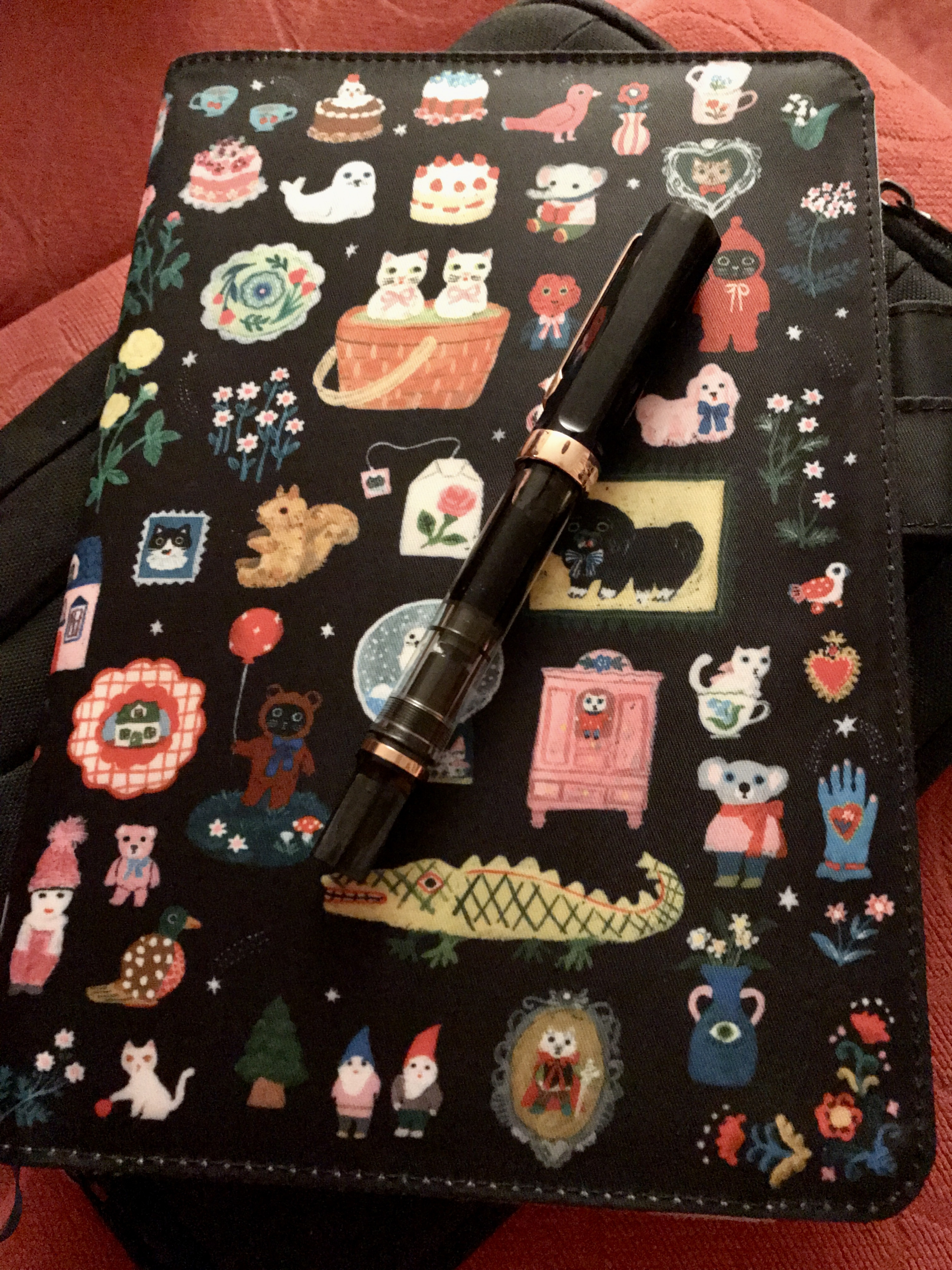 Hobonichi planner plus fountain pen A black fountain pen resting on top of a paper planner inside a brightly coloured soft cover decorated with lots of cute designs.
